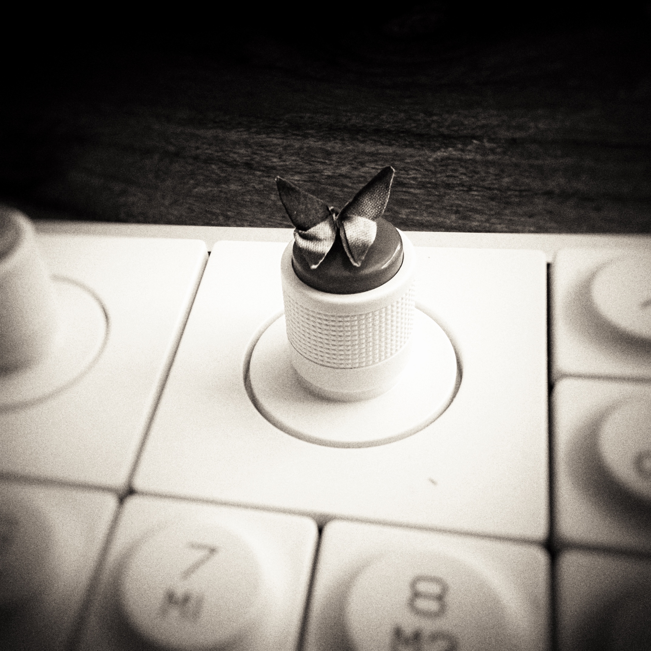 A very tiny origami butterfly on a knob of an OP-1 field with lens blur and vignette.